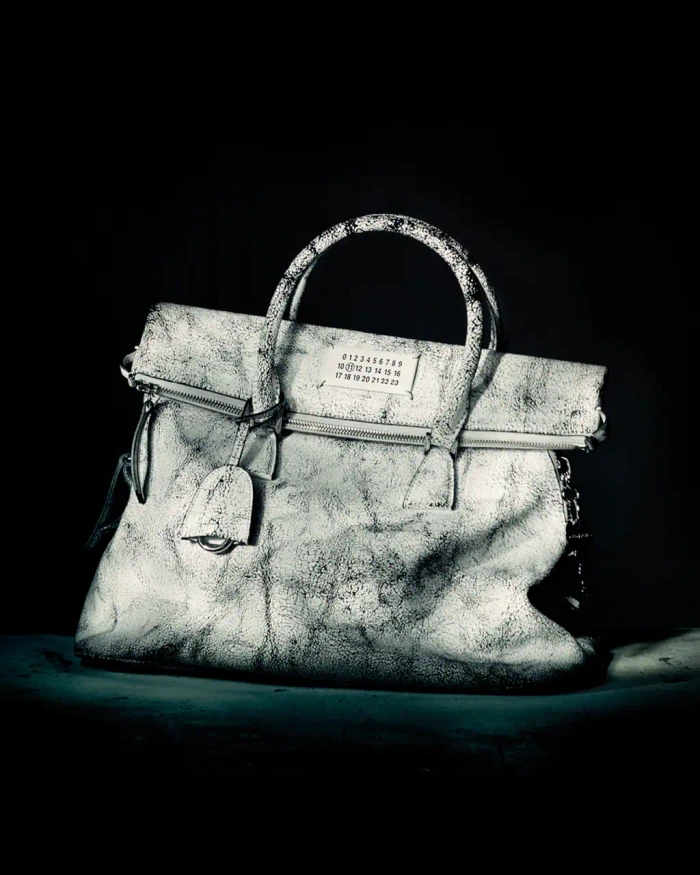 Distressed white leather handbag with top handles and numerical label against dark moody background