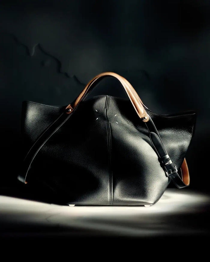 Black leather handbag with tan leather handles centered in a dramatic moody spotlight against a dark textured background.
