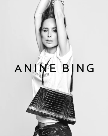 Model with raised arms wearing a white t-shirt and holding a black handbag against a grey seamless background
