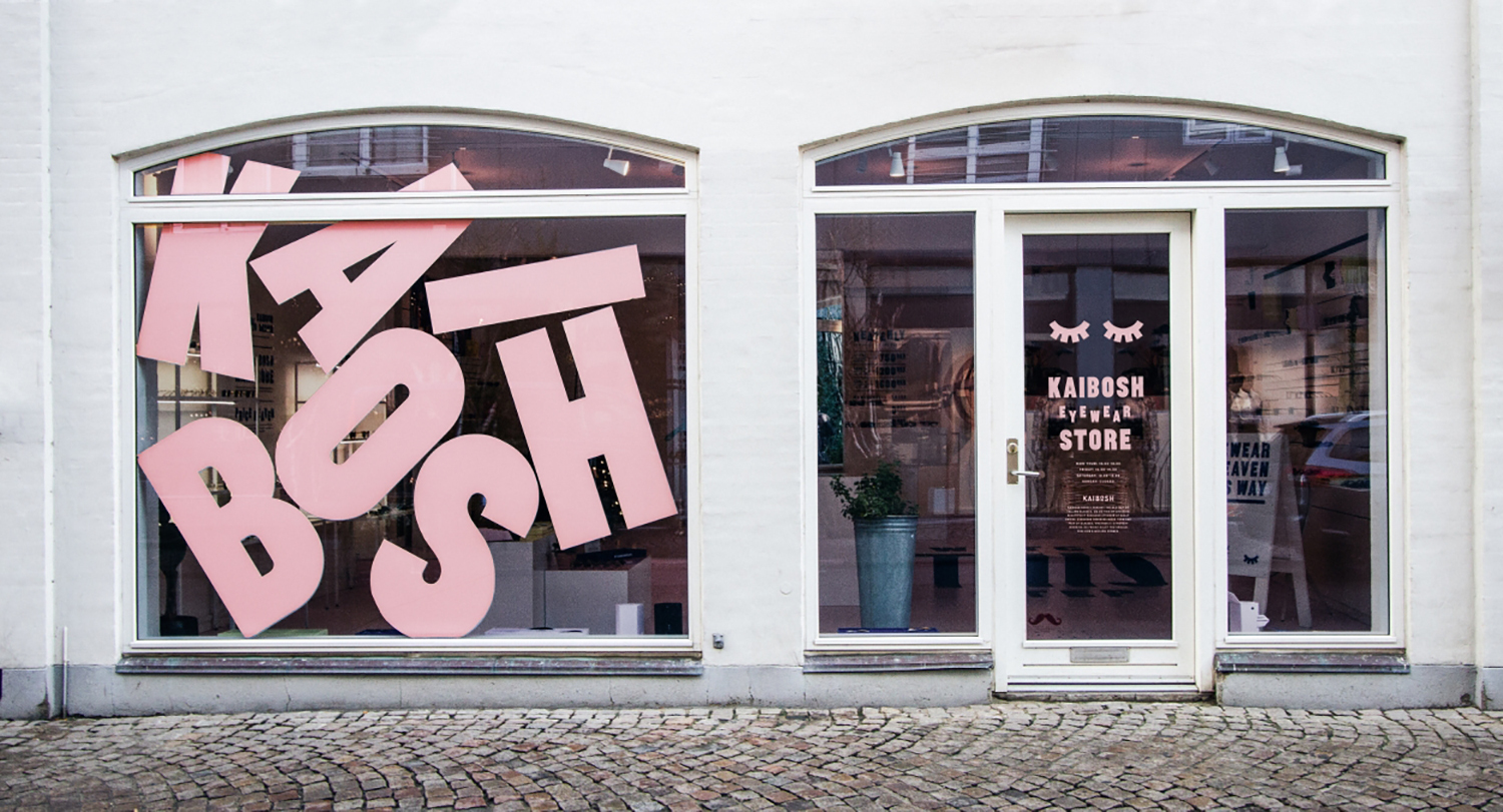 Kaibosh eyewear store exterior with large pink block letters on the window and a cobblestone street.