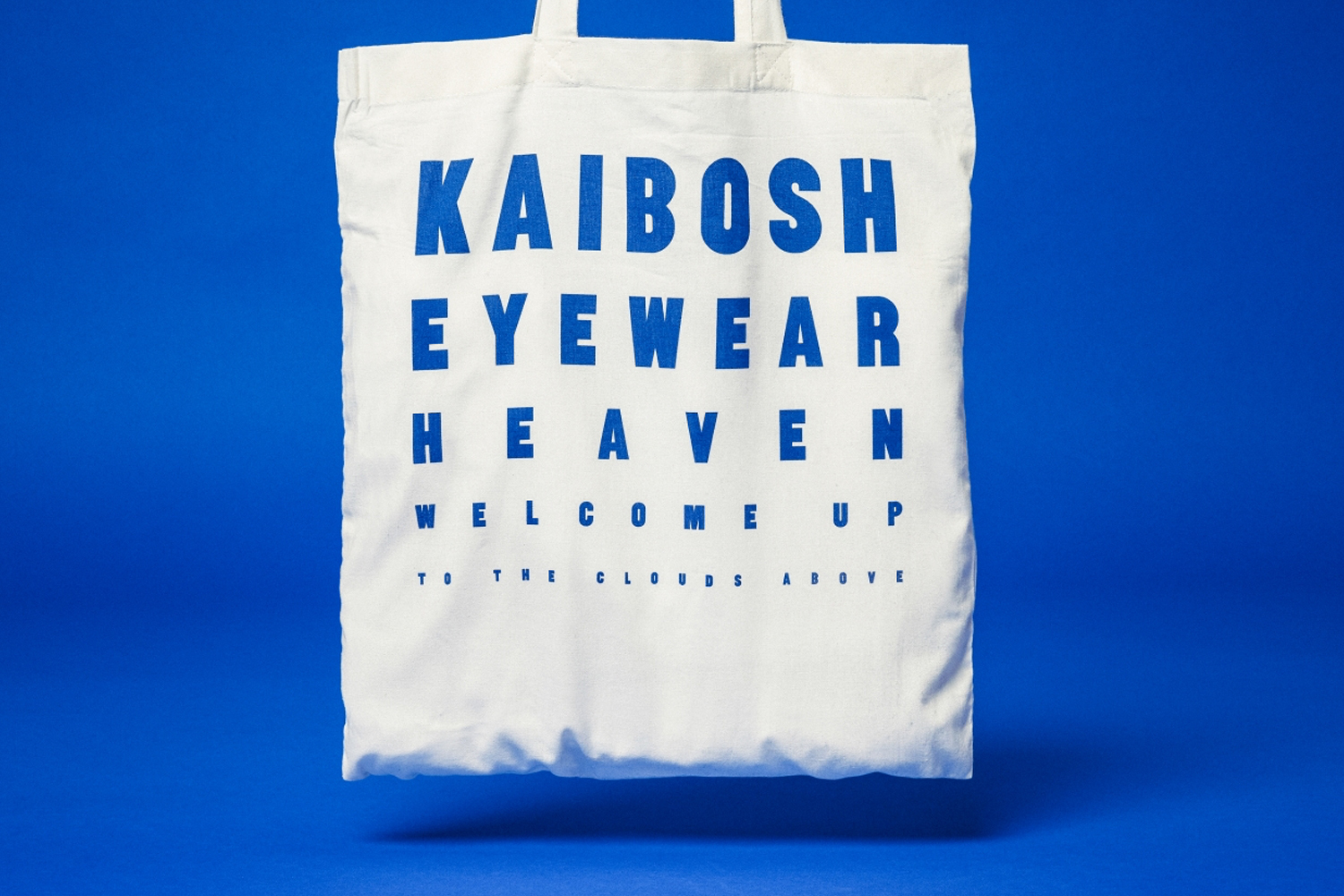 White canvas tote bag featuring blue typography displayed against a solid vibrant blue backdrop.