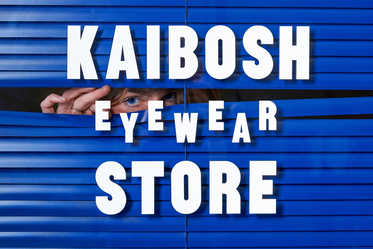 Person looking through blue window blinds with bold white typography overlay for Kaibosh brand identity