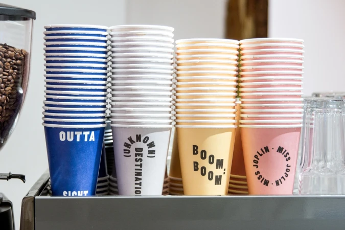 Four stacked columns of colourful paper coffee cups featuring bold typography by Kaibosh