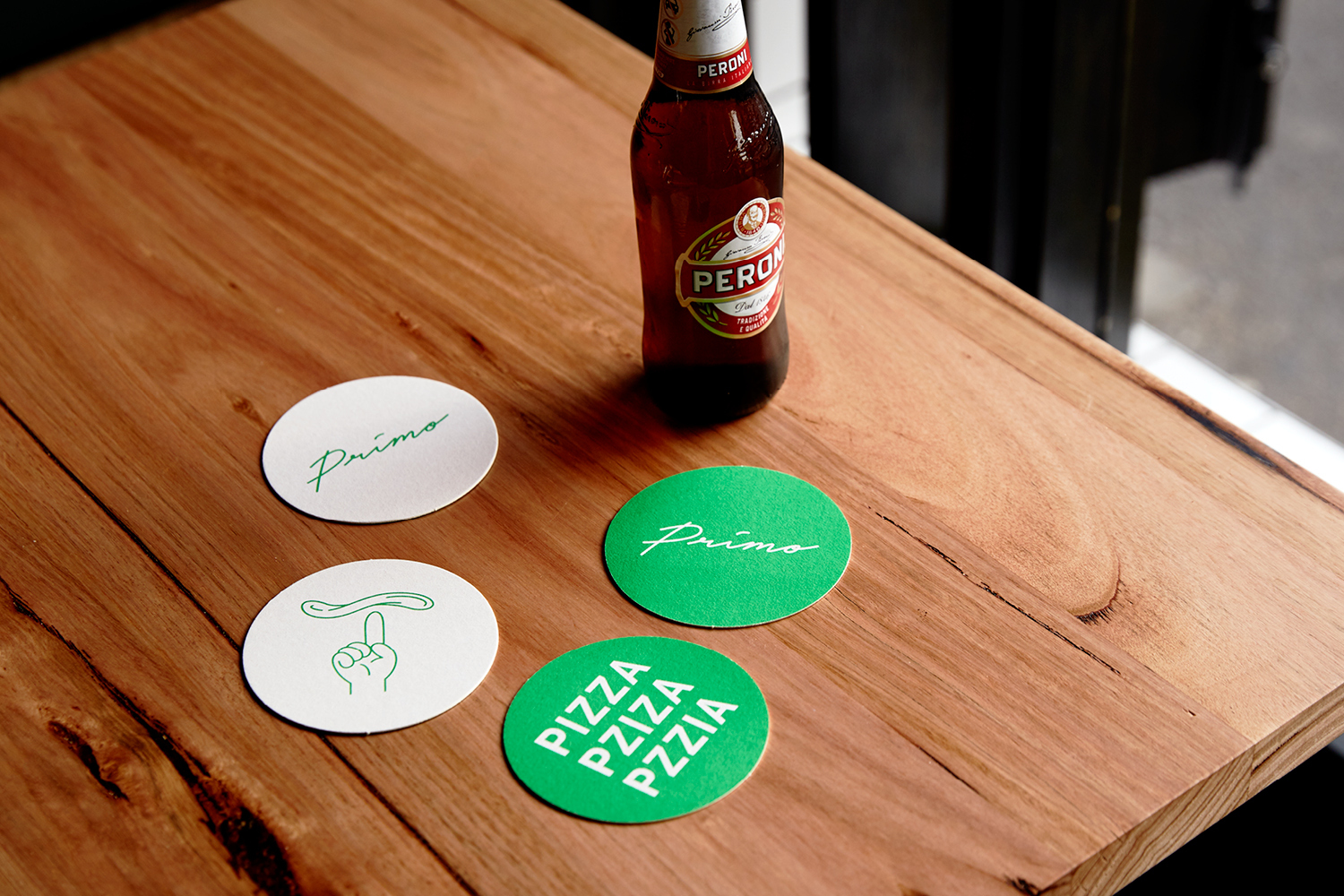 Beer bottle and branded Primo coasters arranged on a wooden table surface
