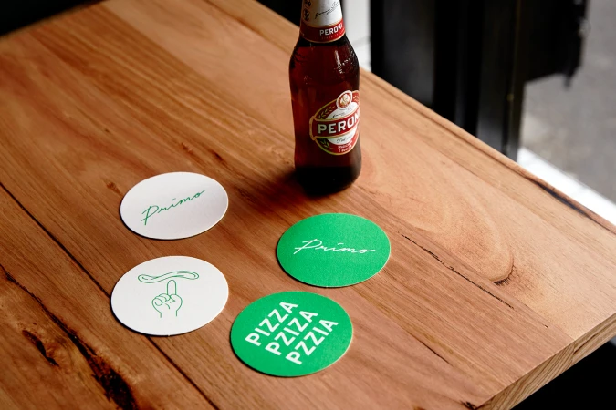 Beer bottle and branded Primo coasters arranged on a wooden table surface