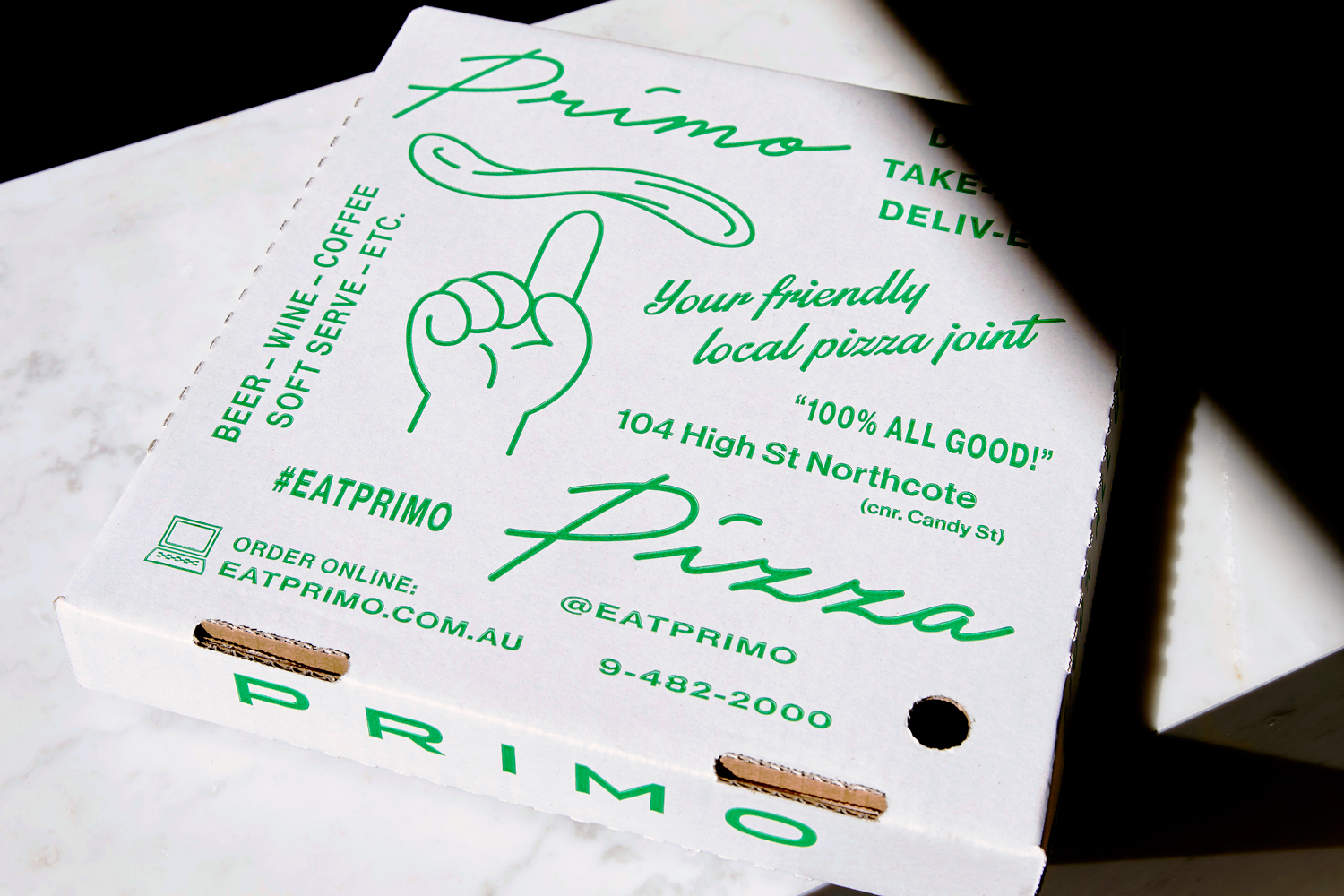 Close-up of a white pizza box with green typography and illustrations, resting on a white marble surface.