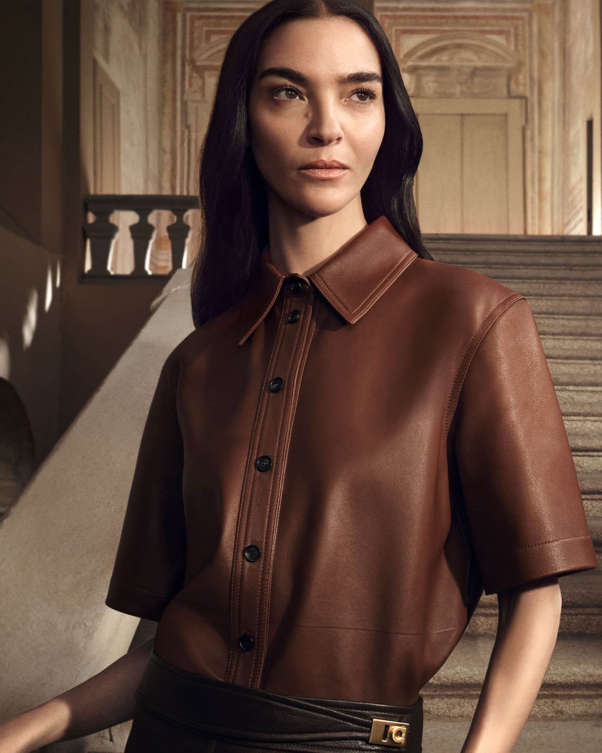 Mariacarla Boscono in a brown leather short-sleeve button-down shirt standing on a stone staircase for Ferragamo Fall 2025 campaign