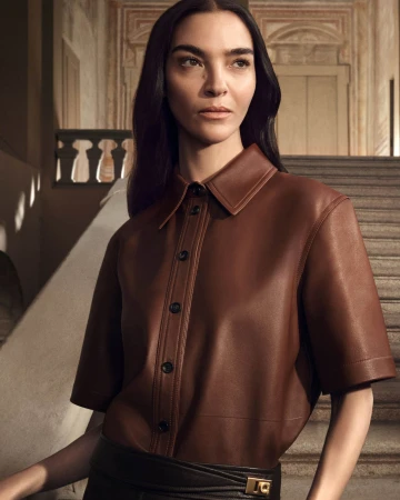 Mariacarla Boscono in a brown leather short-sleeve button-down shirt standing on a stone staircase for Ferragamo Fall 2025 campaign