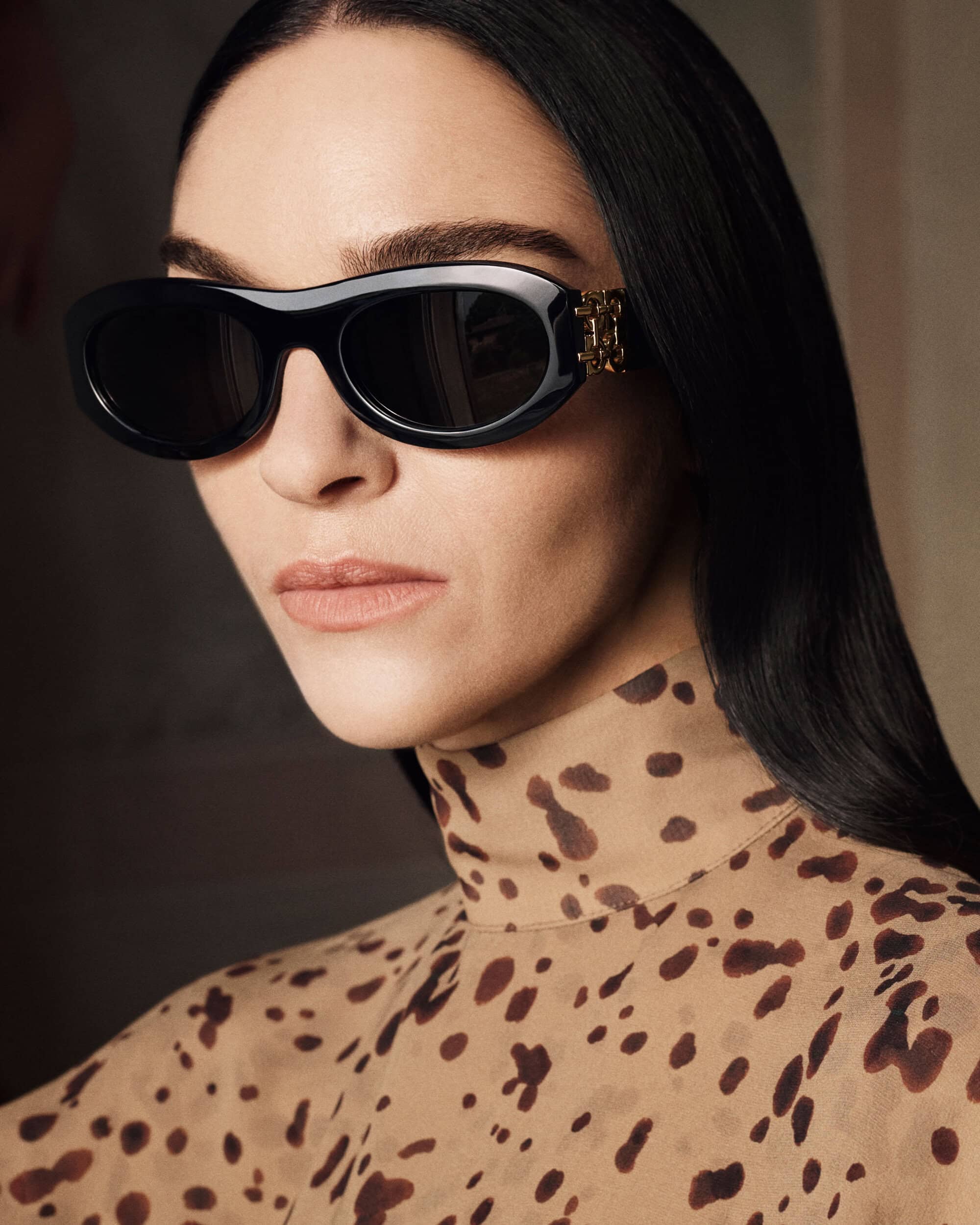 Close-up portrait of a woman wearing black sunglasses and an animal print turtleneck top