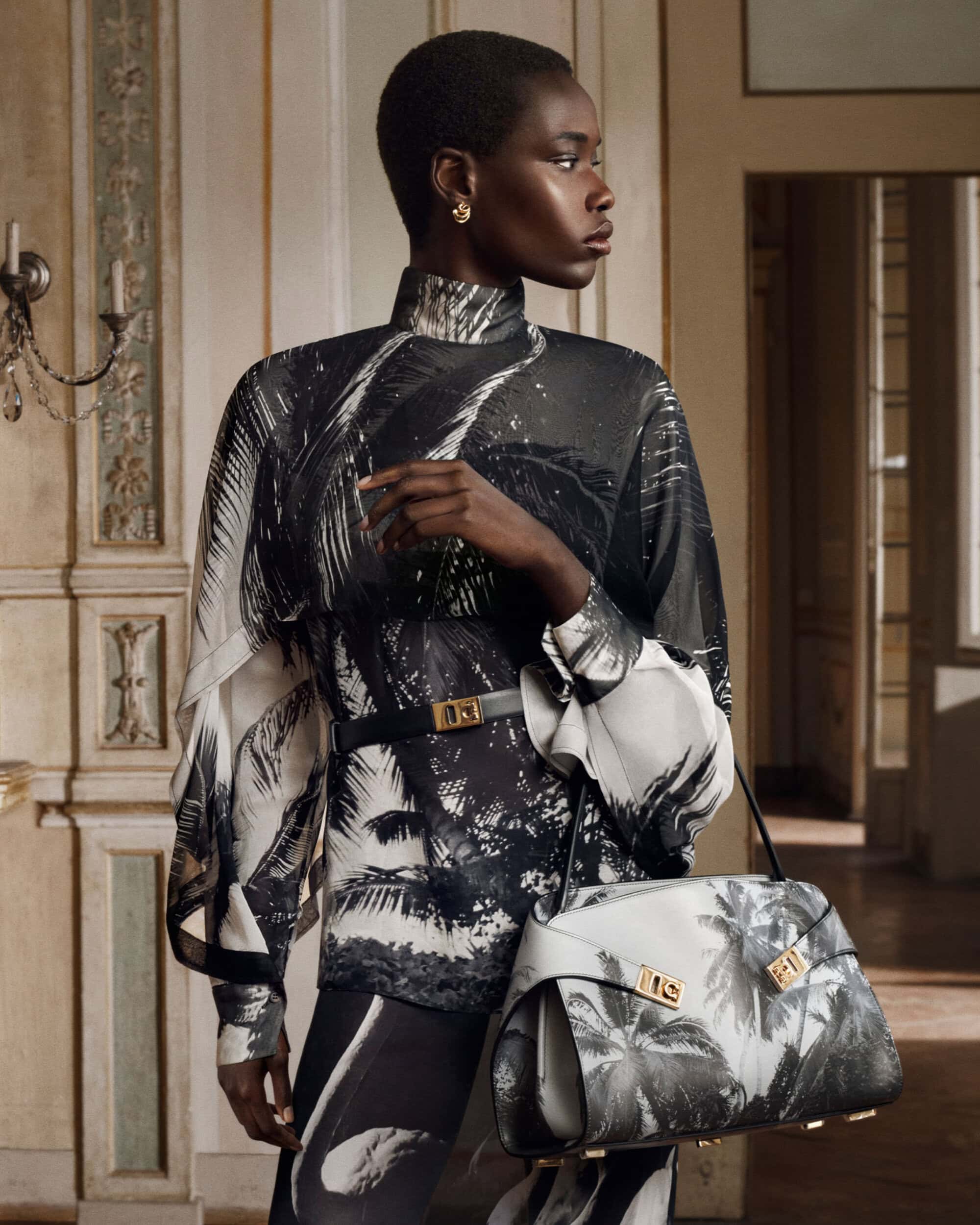Model in black and white printed top holding a matching handbag in an ornate room
