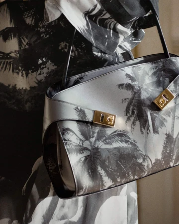 Close-up of a structured black and white palm print handbag with gold hardware held against a matching printed garment