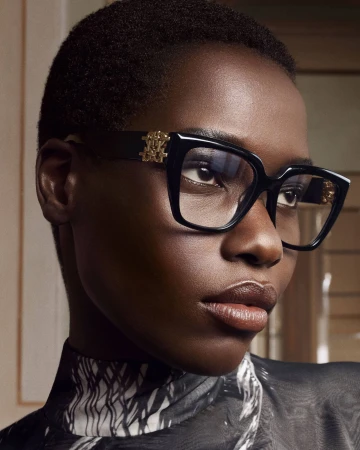 Close-up portrait of a Black woman wearing black designer eyeglasses with gold hardware and a patterned top for Ferragamo Fall 2025.