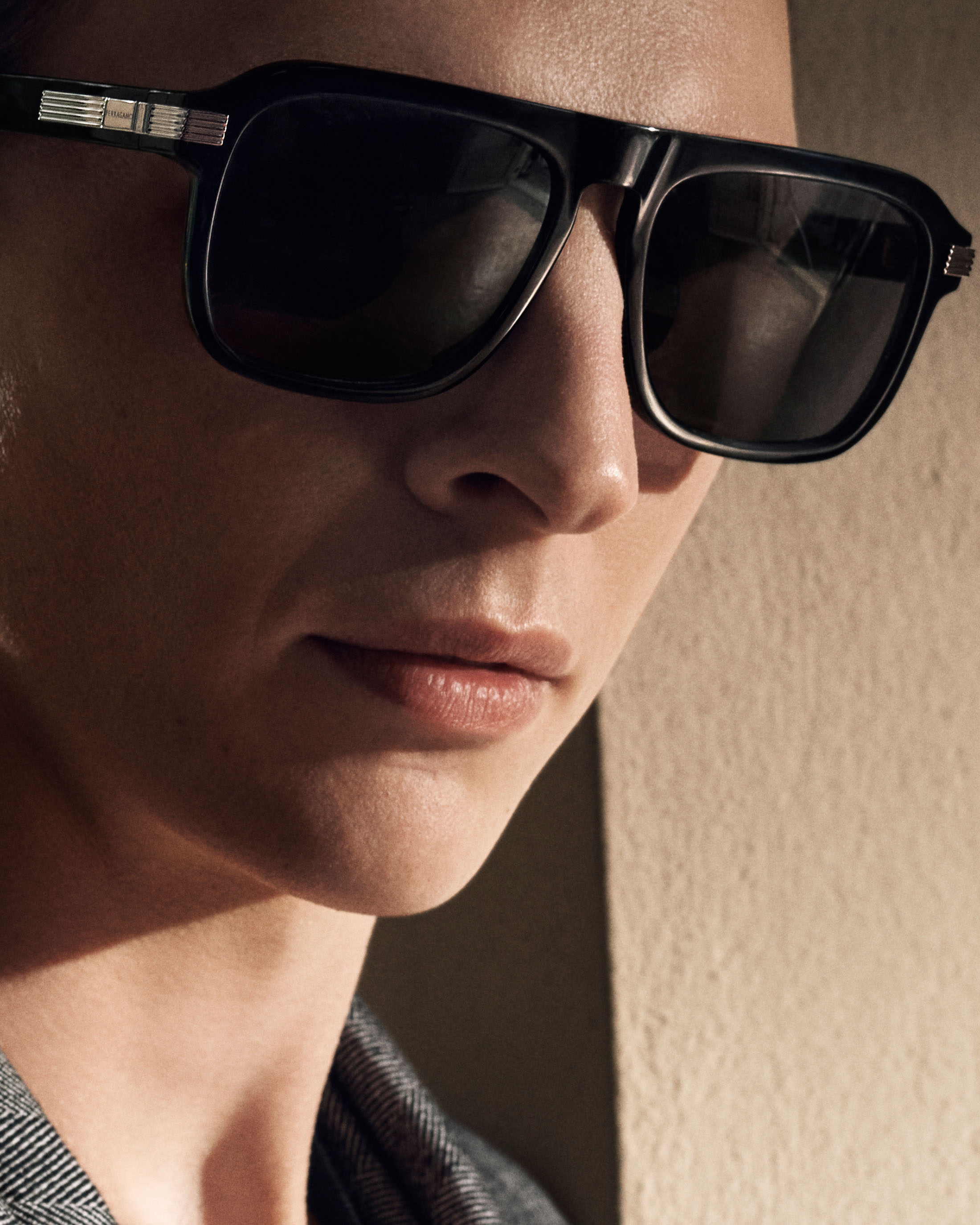 Close-up portrait of a person wearing large black sunglasses and a patterned grey jacket in warm directional light.