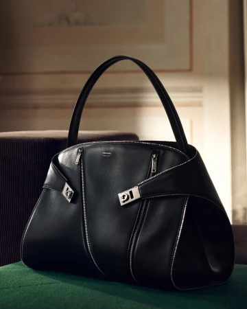 Black leather handbag with silver hardware resting on a dark green surface against an interior background