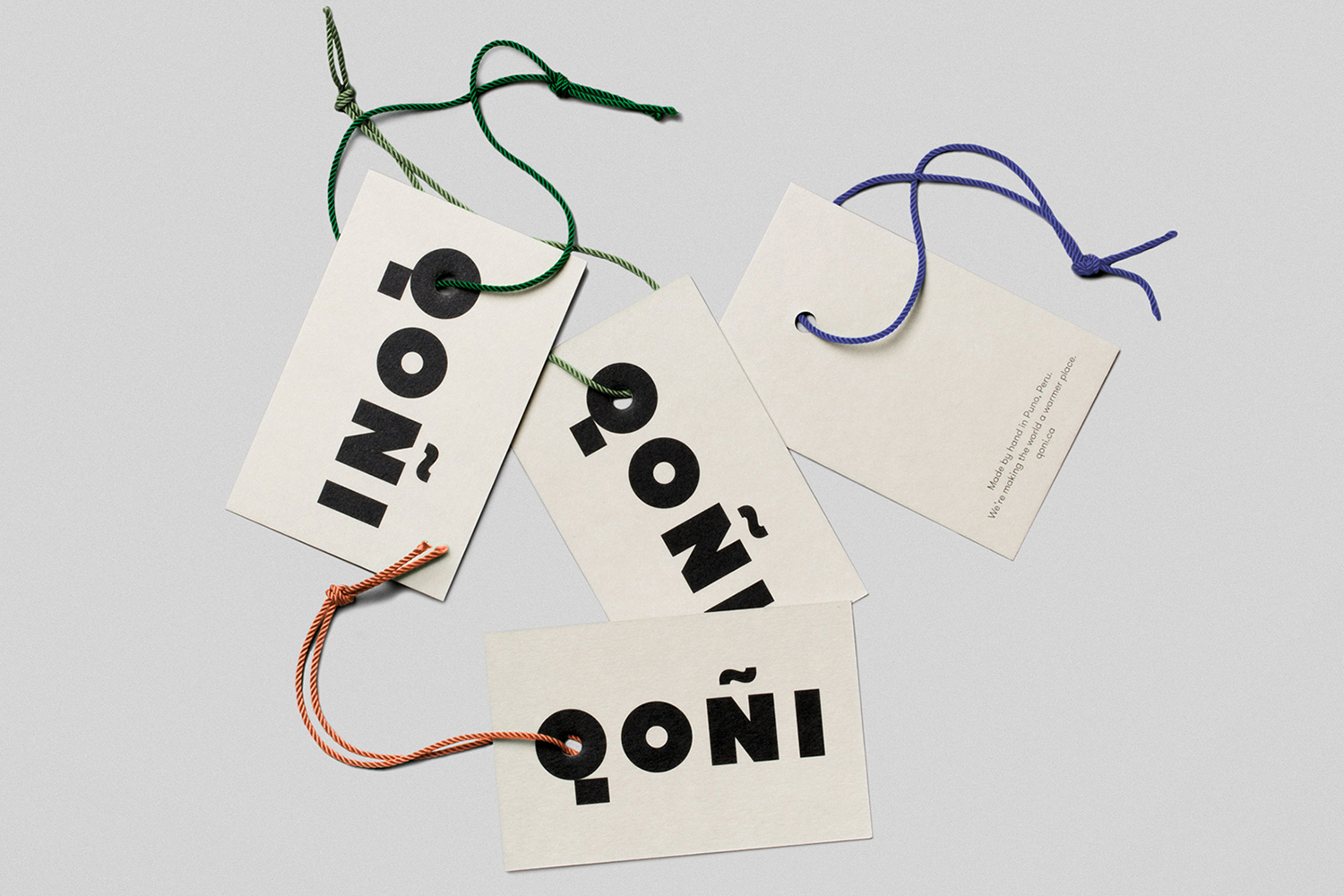 Four white paper swing tags with bold black Qoni branding and colourful string cords on a grey background
