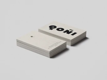 Two stacked white business cards with bold black typography resting on a neutral gray studio surface