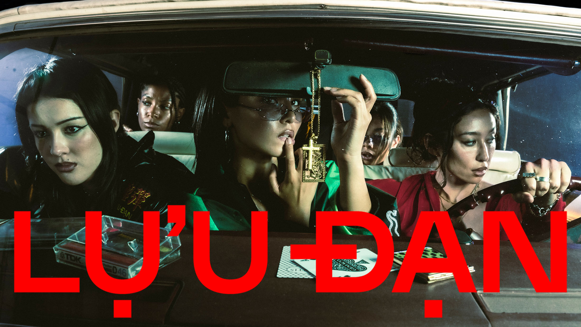 Five models seated inside a vintage car at night, captured in a cinematic promotional campaign shot for Lu'u Dan Fall 2025.