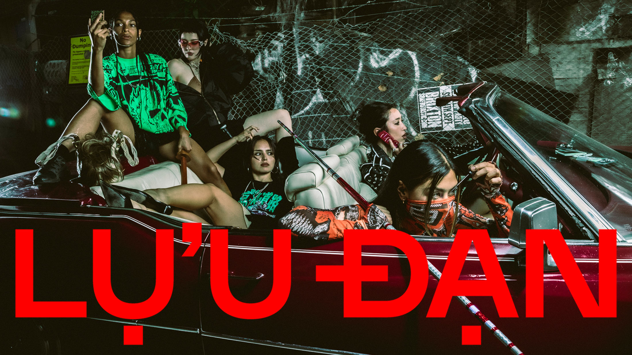Five models posing inside and around a maroon convertible car against a chain link fence backdrop for Lu'u Dan