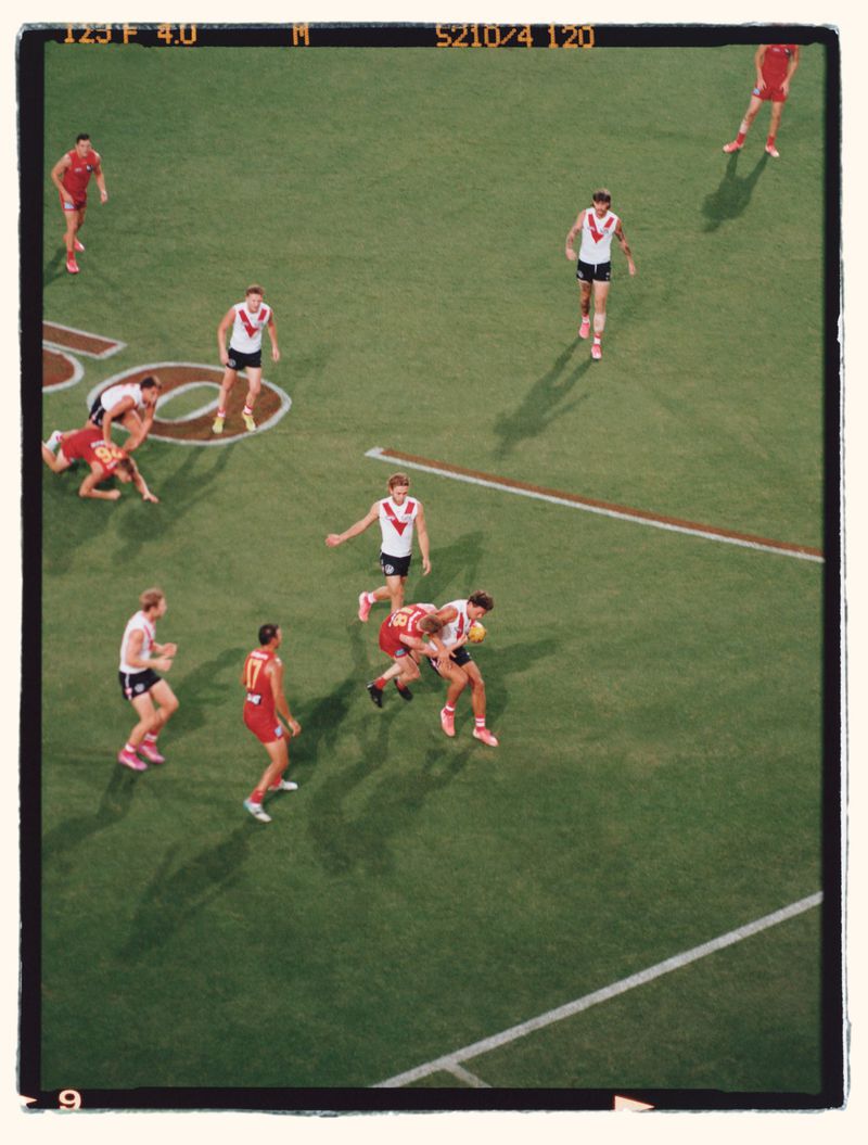 Action shot of an Australian Rules football game on a green field under bright lighting with players in red and white uniforms.