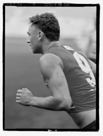 Monochrome photo of a man running in athletic attire with a number on his back, captured outdoors with a focus on fitness and sport.