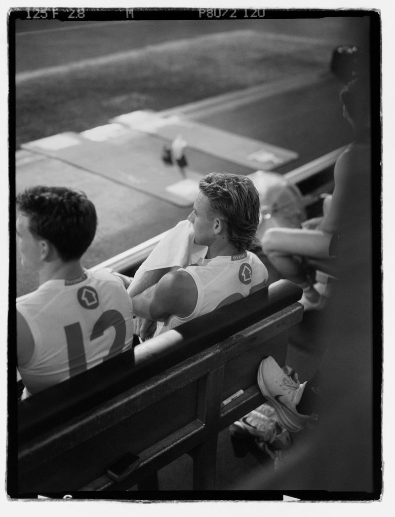 Monochrome shot of two people in sports uniforms sitting on a bench in an outdoor setting, captured with a medium framing angle.