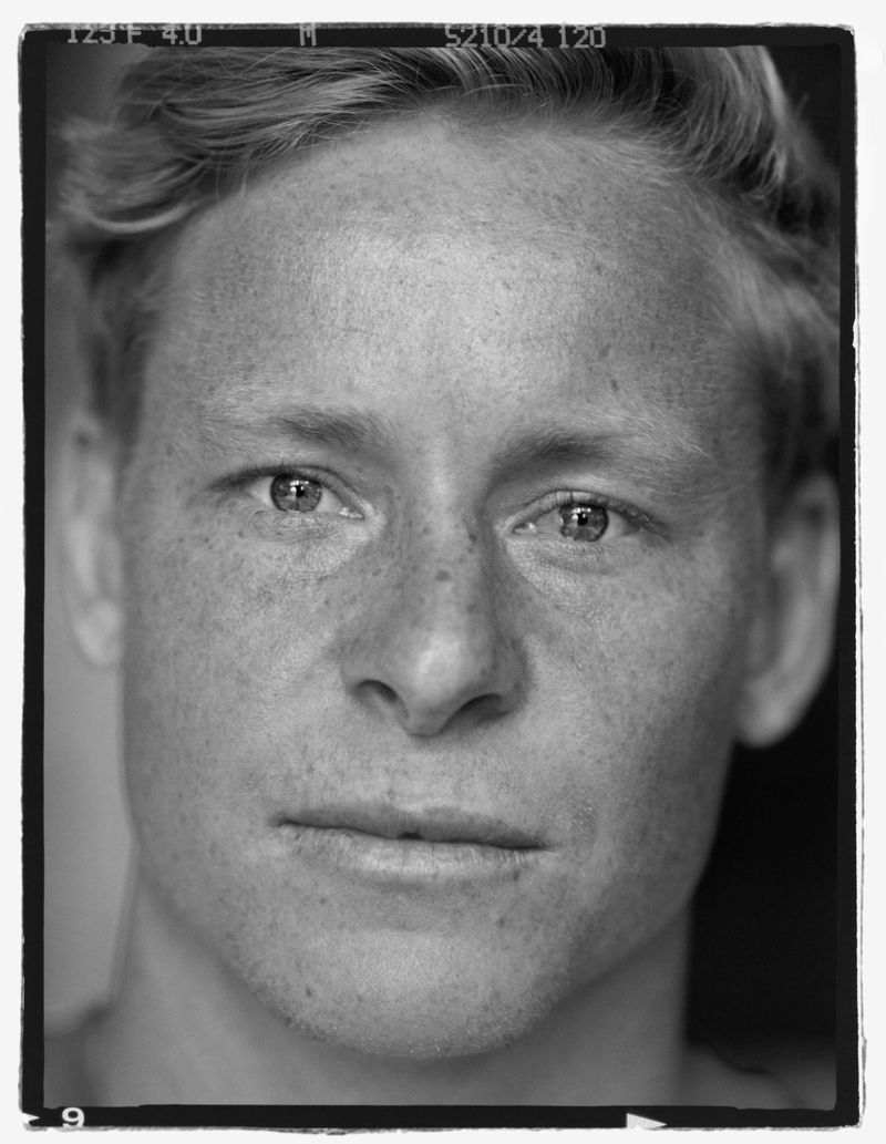 Close-up black and white portrait of a fair-skinned adult male with short blond hair looking directly at the camera with a neutral expression.