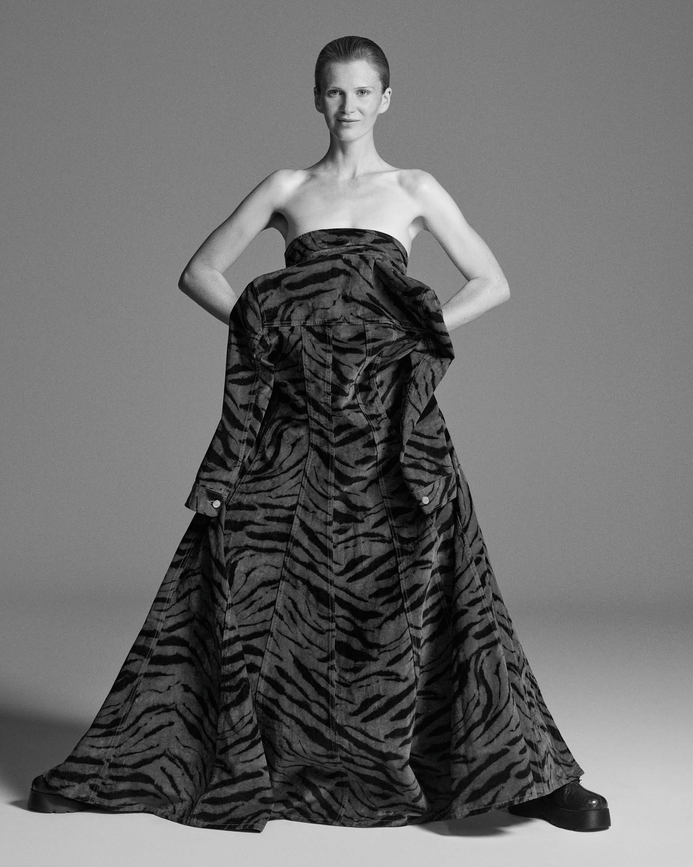 Model wearing a strapless dark patterned gown standing against a plain grey backdrop for Ganni fall 2025 ad campaign.