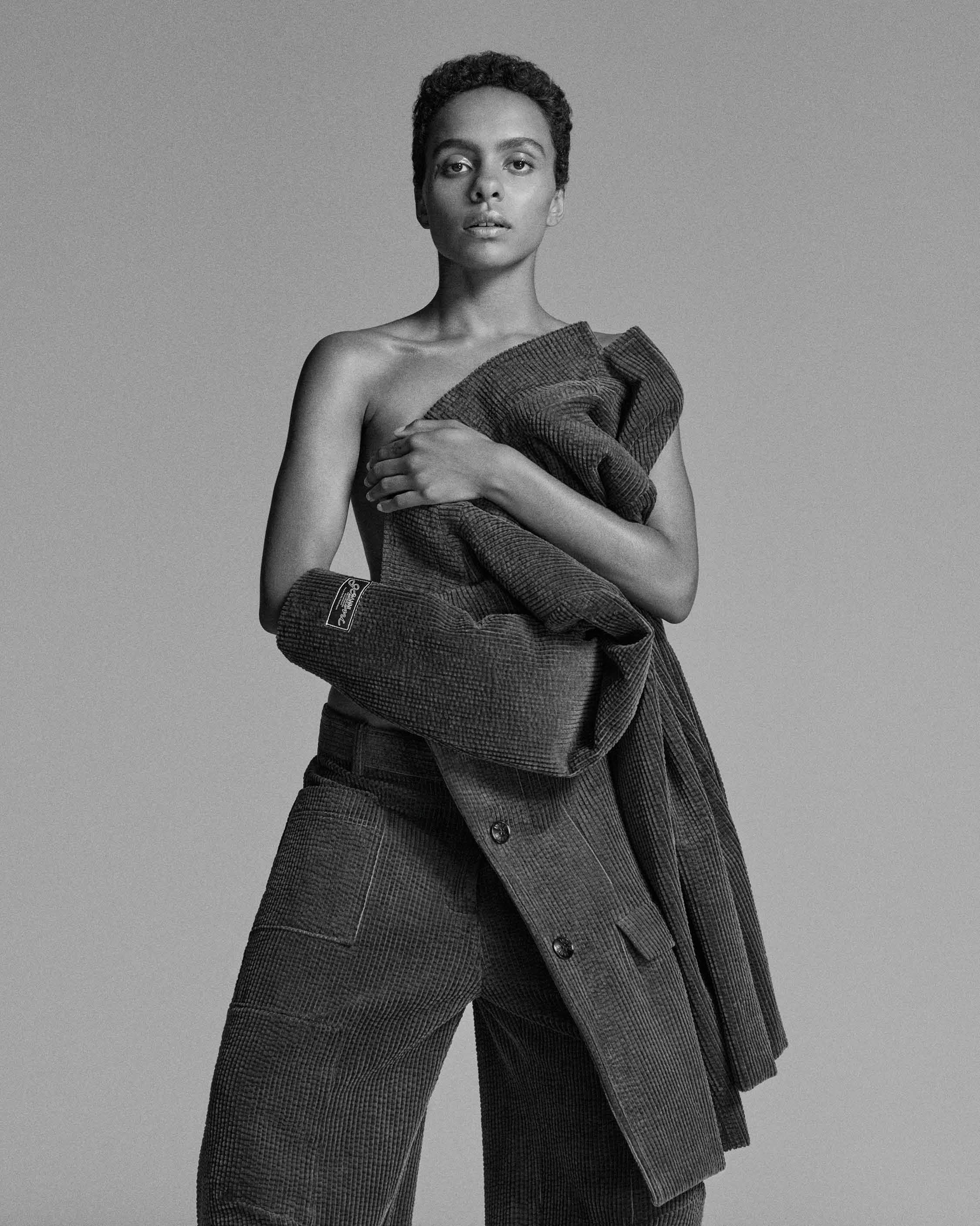 Black and white studio portrait of a woman holding a textured coat against her chest against a grey background