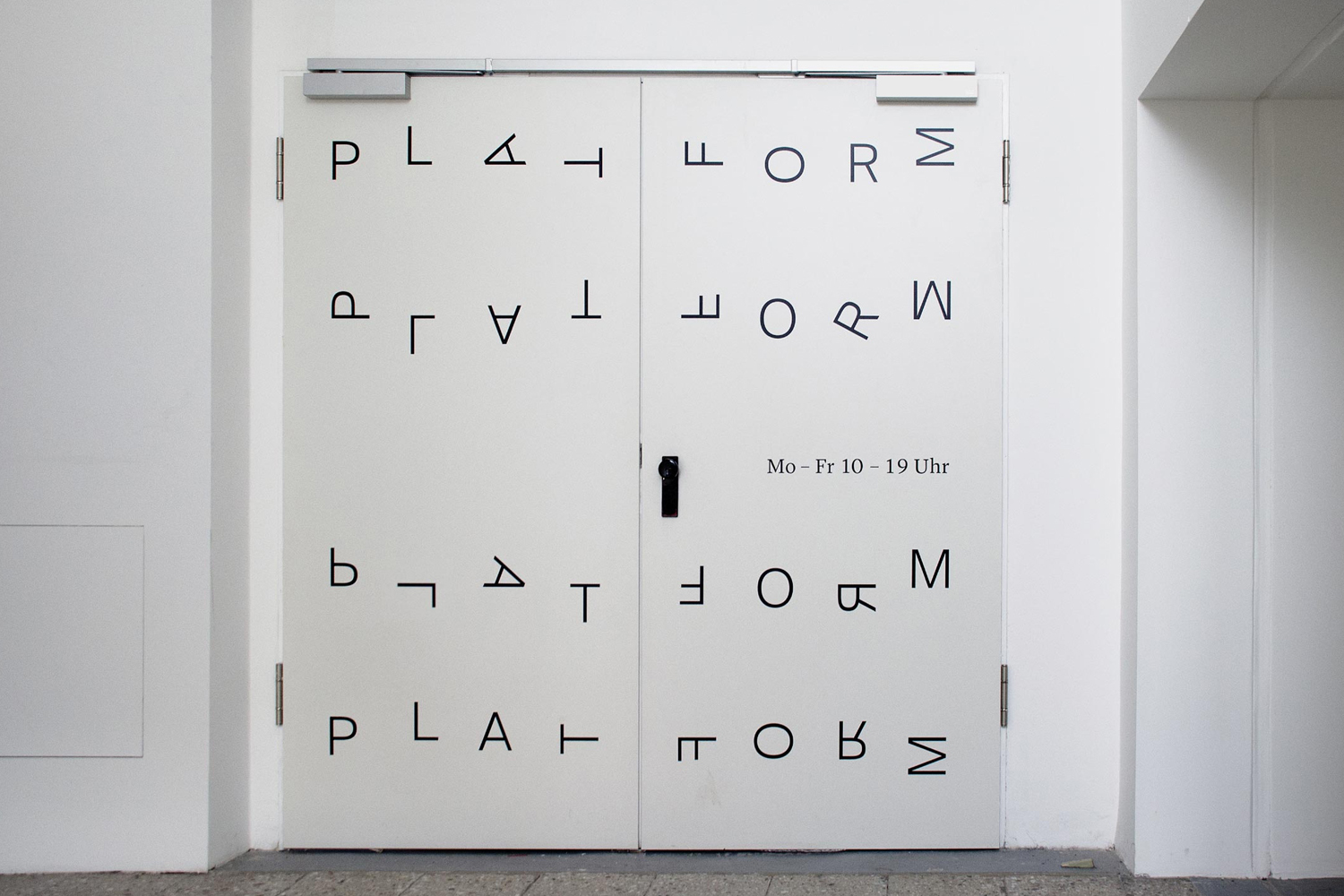 Double doors featuring minimalist typographic branding with rotated and mirrored black letters spelling Platform against a white wall.