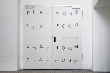 Double doors featuring minimalist typographic branding with rotated and mirrored black letters spelling Platform against a white wall.