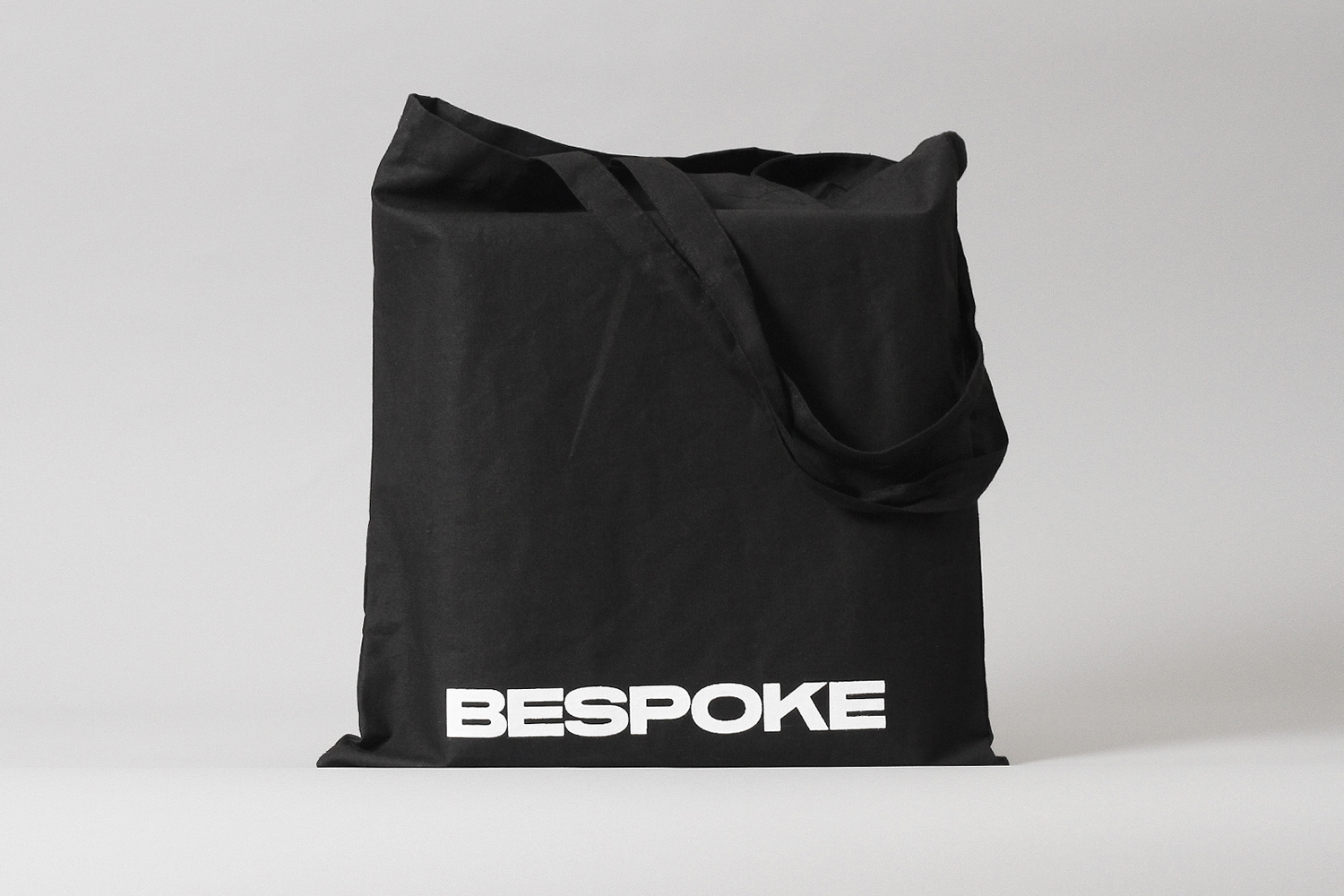 Black canvas tote bag with white Bespoke typography resting against a neutral grey studio background