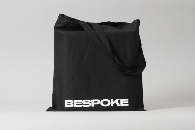 Black canvas tote bag with white Bespoke typography resting against a neutral grey studio background
