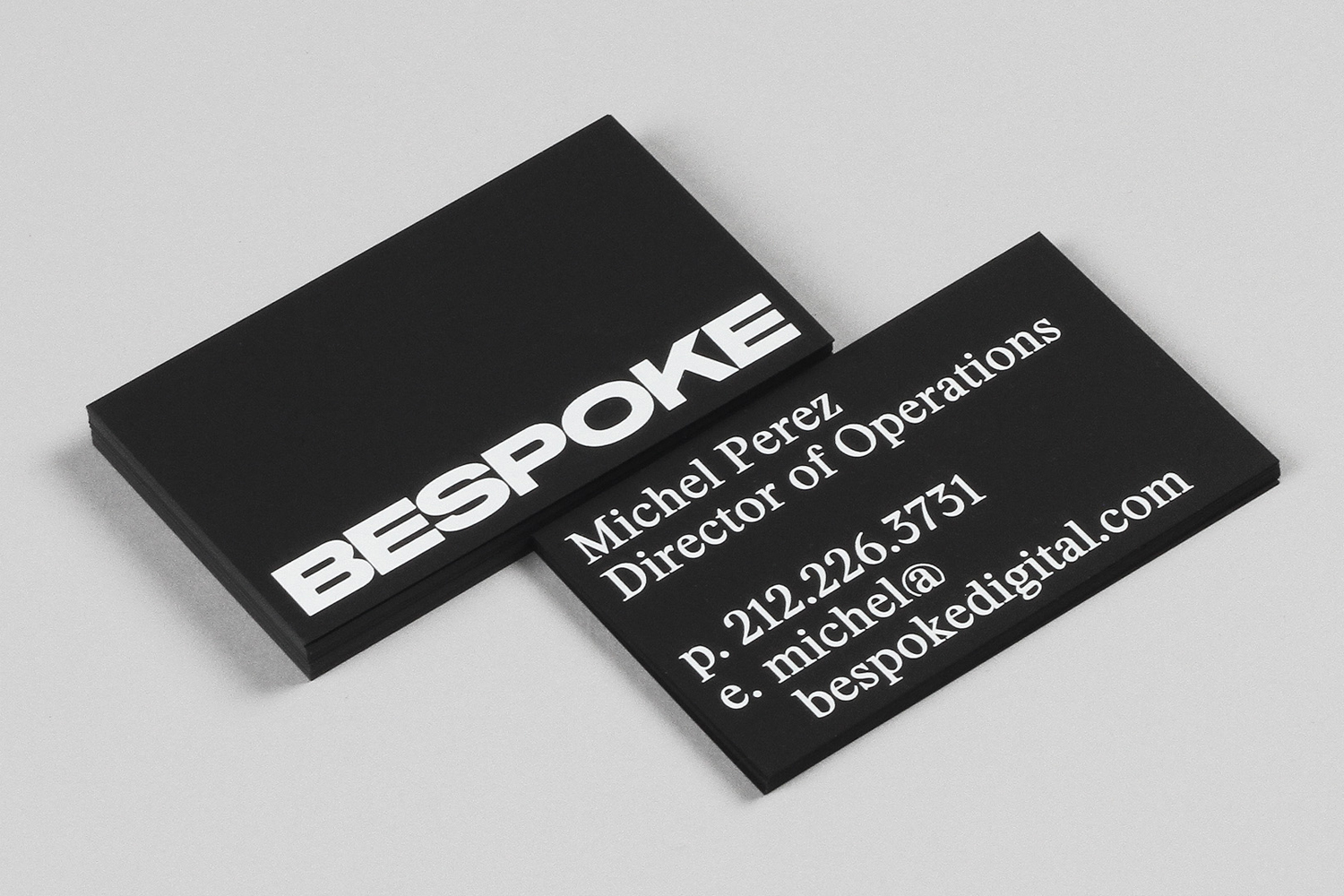 Two black business cards with white typography angled on a light grey studio background for Bespoke brand identity