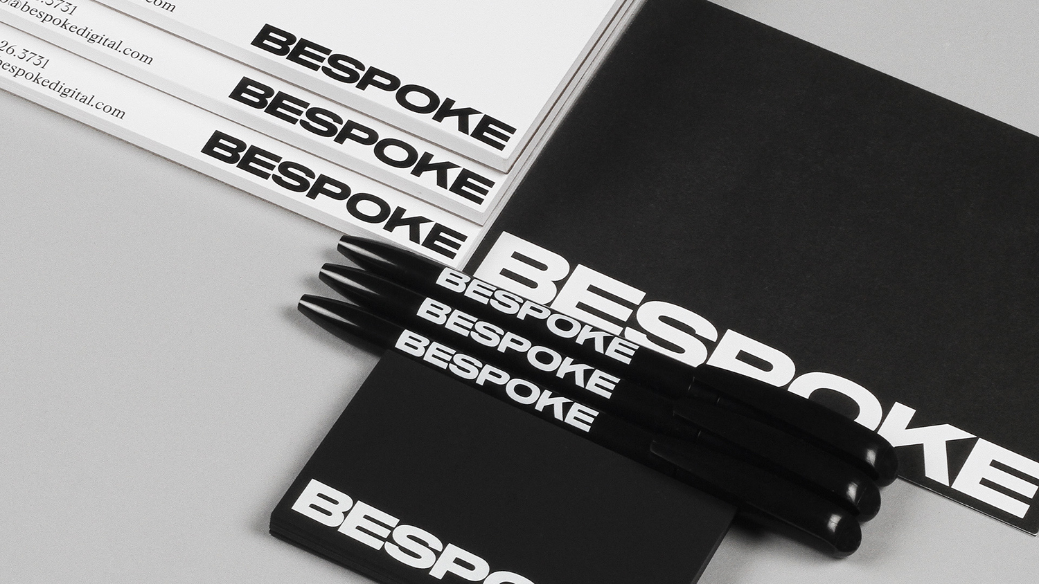 Bespoke brand identity stationery flat lay with black pens, notebooks, and letterhead featuring bold typography.