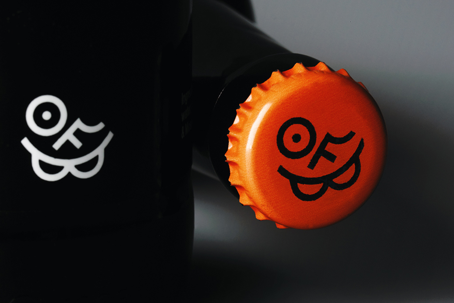 Close-up product shot of a black beer bottle with a bright orange bottle cap featuring a custom logo