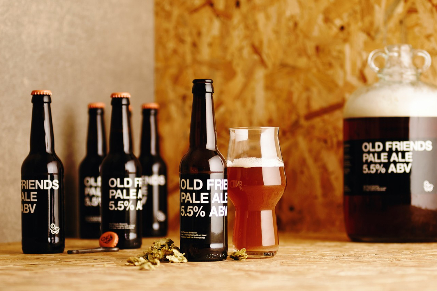 Several dark glass beer bottles with white text labels and a filled beer glass placed on a wooden textured tabletop