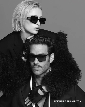 Paris Hilton and Jon Kortajarena wearing sunglasses and black outerwear in a monochrome fashion campaign ad portrait