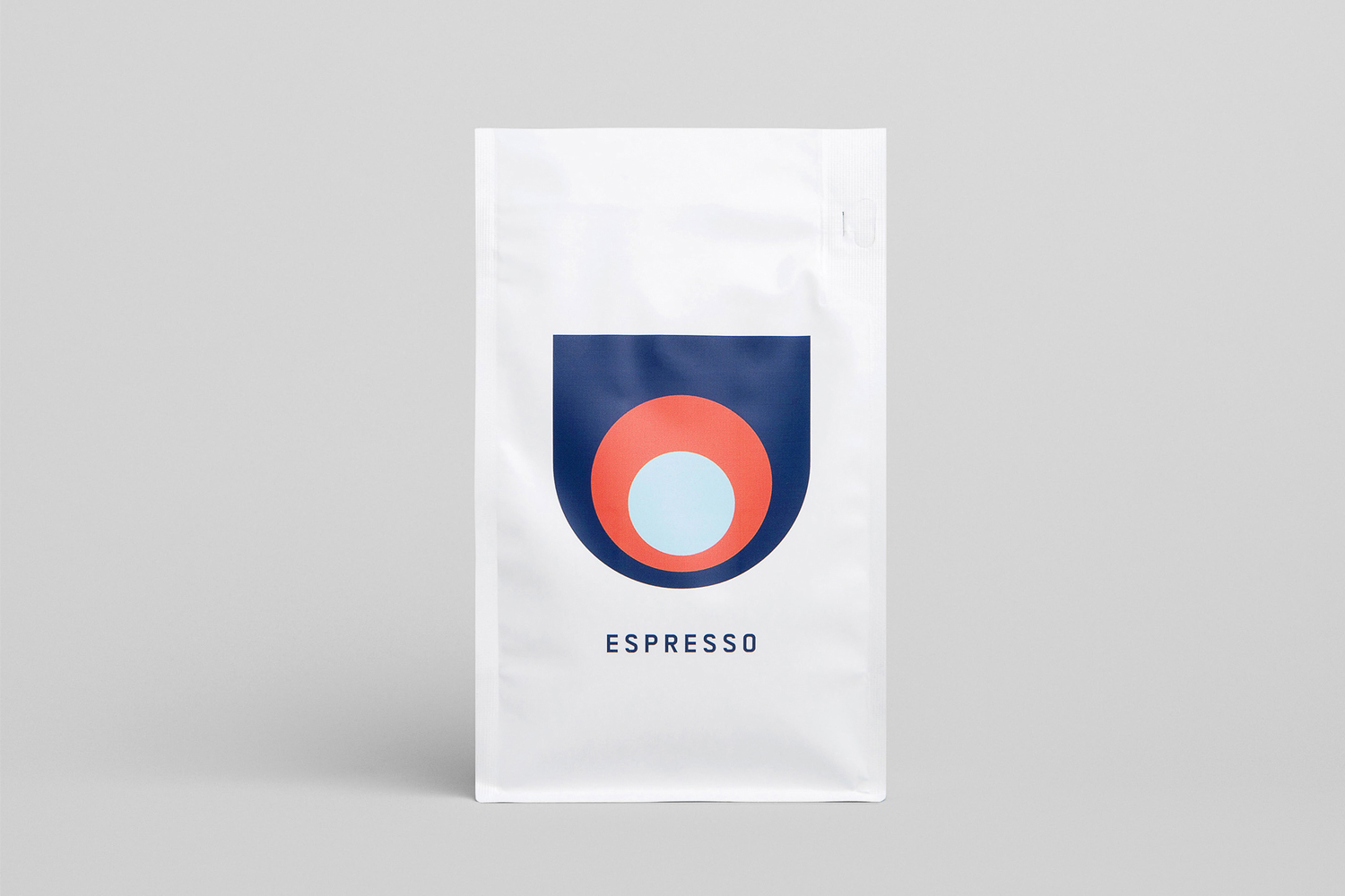 White Deluca Coffee espresso bag featuring a geometric logo design against a seamless neutral grey background