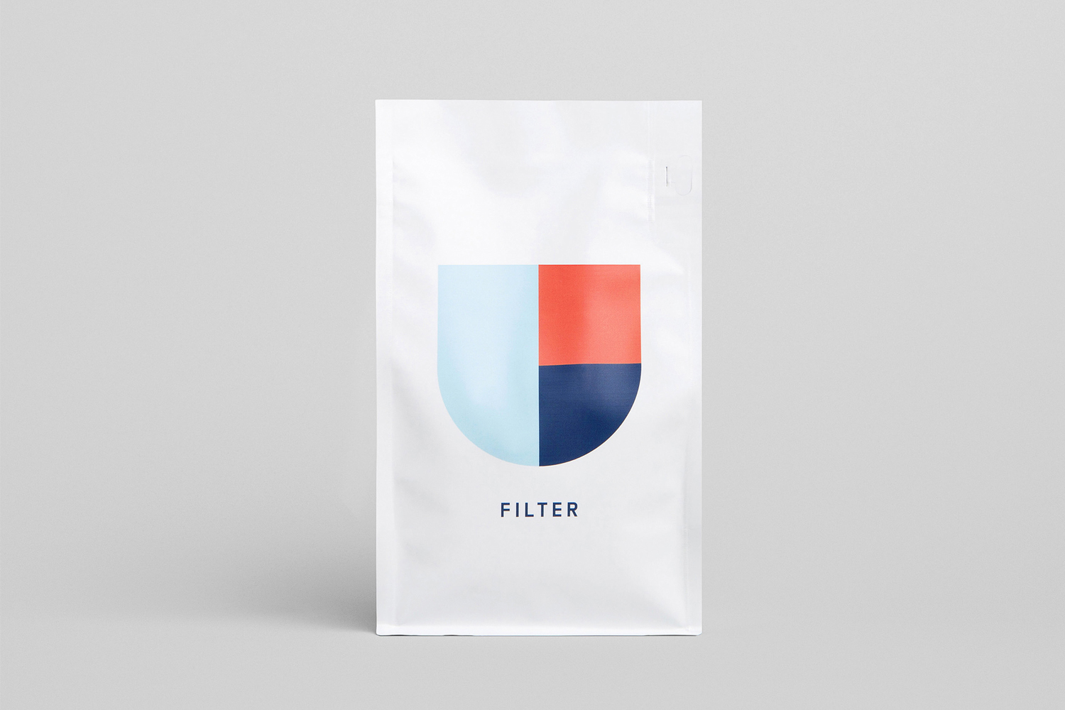 Glossy white coffee bag packaging featuring a geometric U-shaped logo and the word FILTER against a seamless grey backdrop.