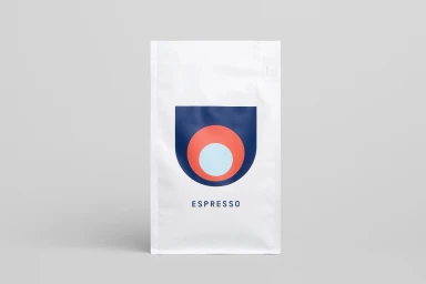 White Deluca Coffee espresso bag featuring a geometric logo design against a seamless neutral grey background