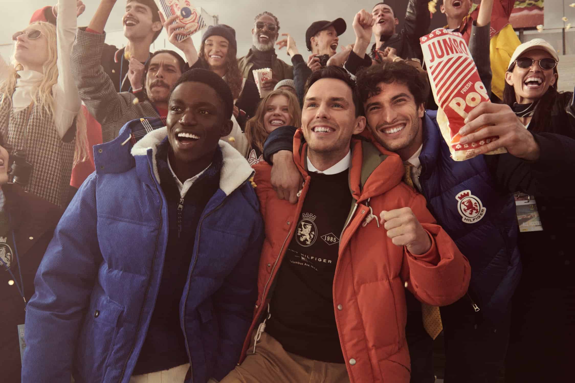 Diverse group of smiling people cheering together in outerwear, holding popcorn bags outdoors during an event.
