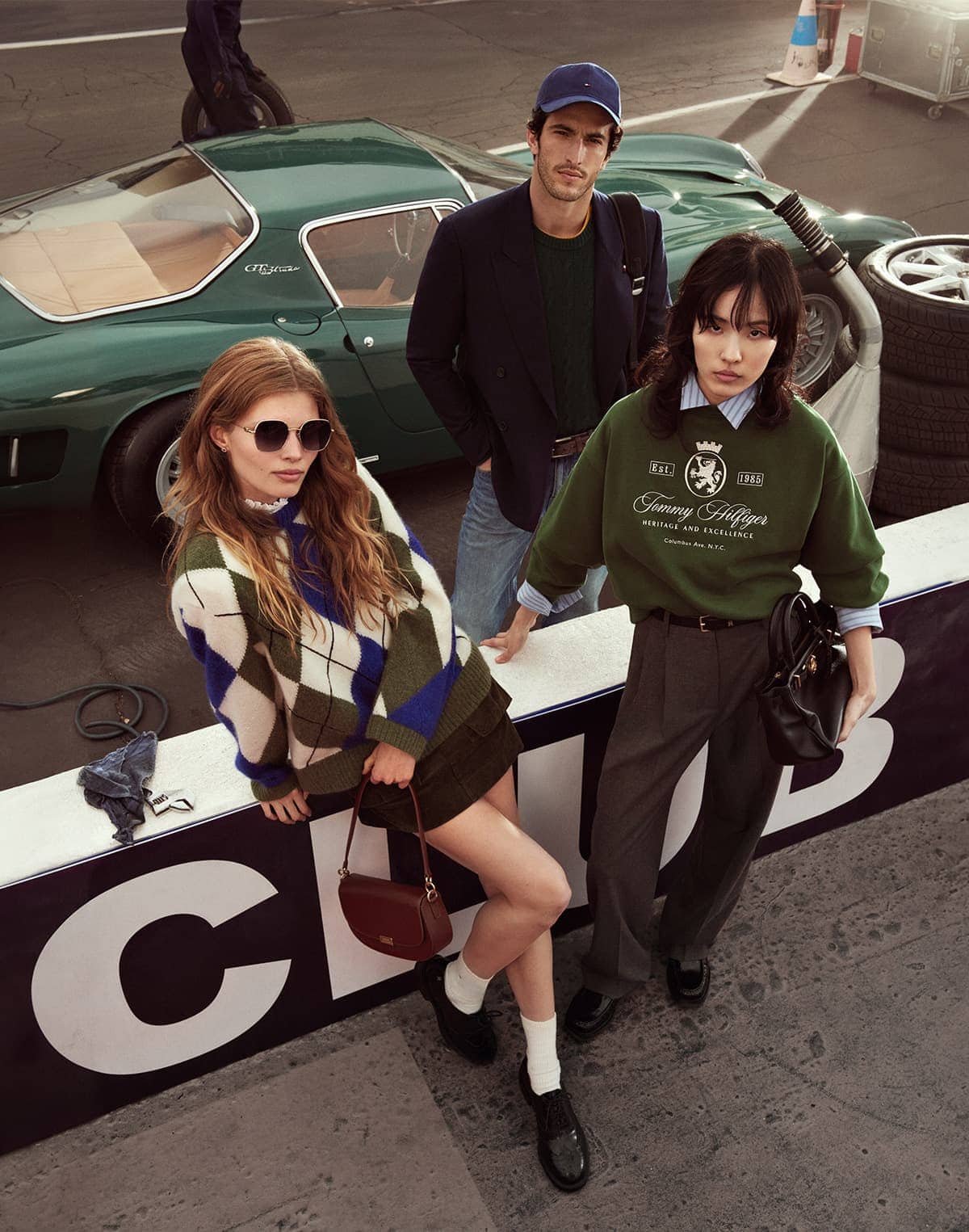 Three models posing outdoors near a classic green sports car for Tommy Hilfiger Fall 2025 ad campaign.