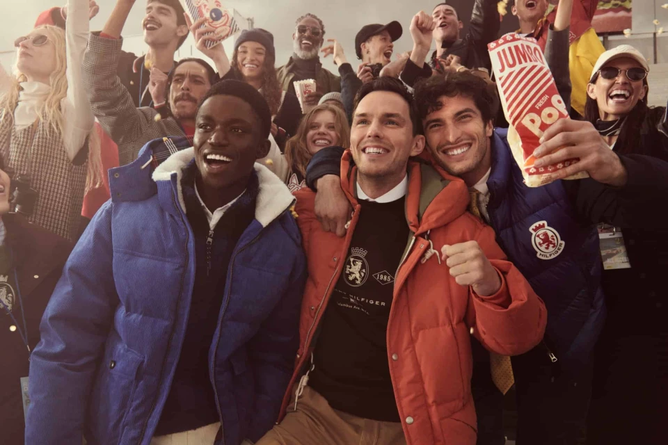 Diverse group of smiling people cheering together in outerwear, holding popcorn bags outdoors during an event.