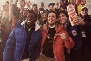 Diverse group of smiling people cheering together in outerwear, holding popcorn bags outdoors during an event.