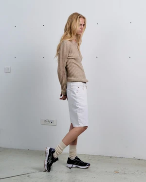 Model in ribbed beige sweater and white shorts posing against a plain wall for M Le magazine du Monde