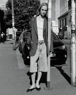 Model Rikke Nora Palsgaard Ronne in an oversized blazer and denim shorts leaning against a pole on a city street.