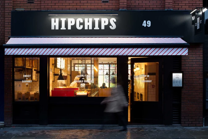 Exterior storefront of Hipchips restaurant with bold black signage, red-and-white striped awning, and brick building facade