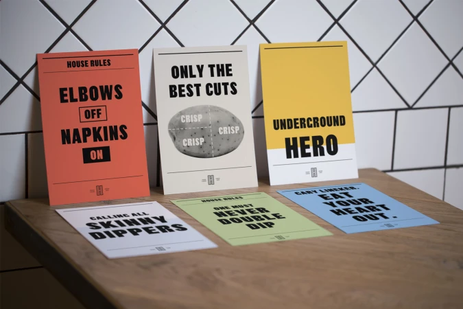 Colorful printed cards with bold typography displayed on a wooden surface against a tiled wall