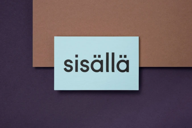 Blue business card featuring the black text sisällä resting on layered brown and dark purple paper backgrounds