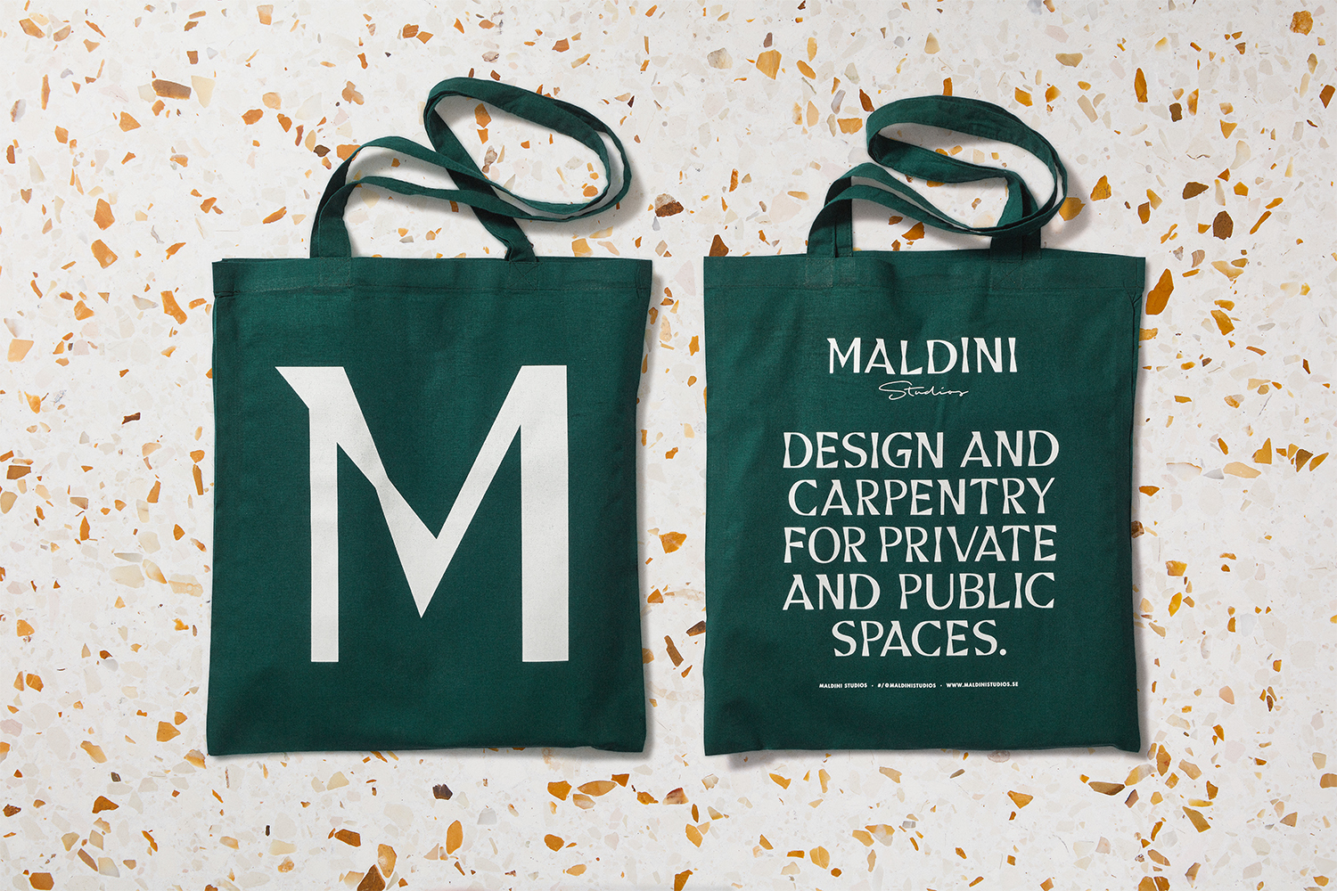 Two dark green canvas tote bags featuring white typography displayed flat on a terrazzo surface.